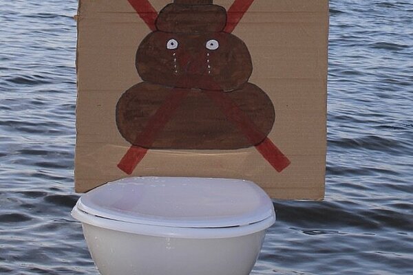 A cardboard sign of a crossed through poop emoji on a toilet in the sea